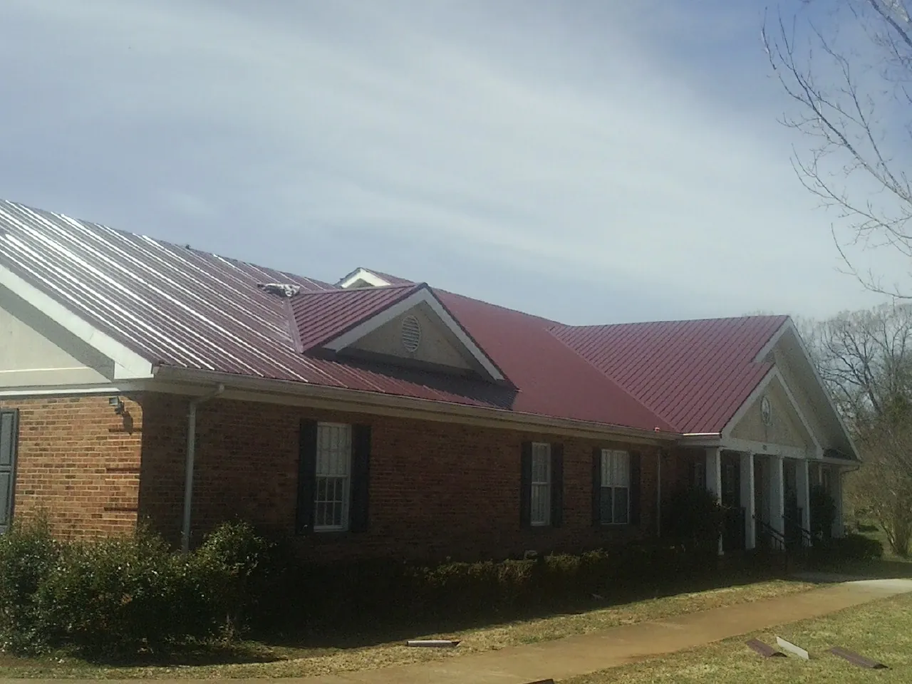 Red metal roof with gabled entries on a long brick building, from a Hail Damage Roof Repair job in Lee Center