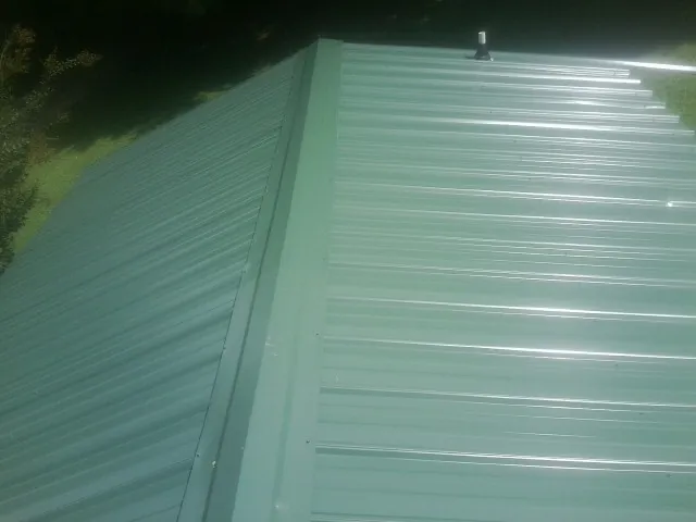 New green metal panels meeting at the ridge of a roof — Flat Roof Repair work by our crew in Lee Center