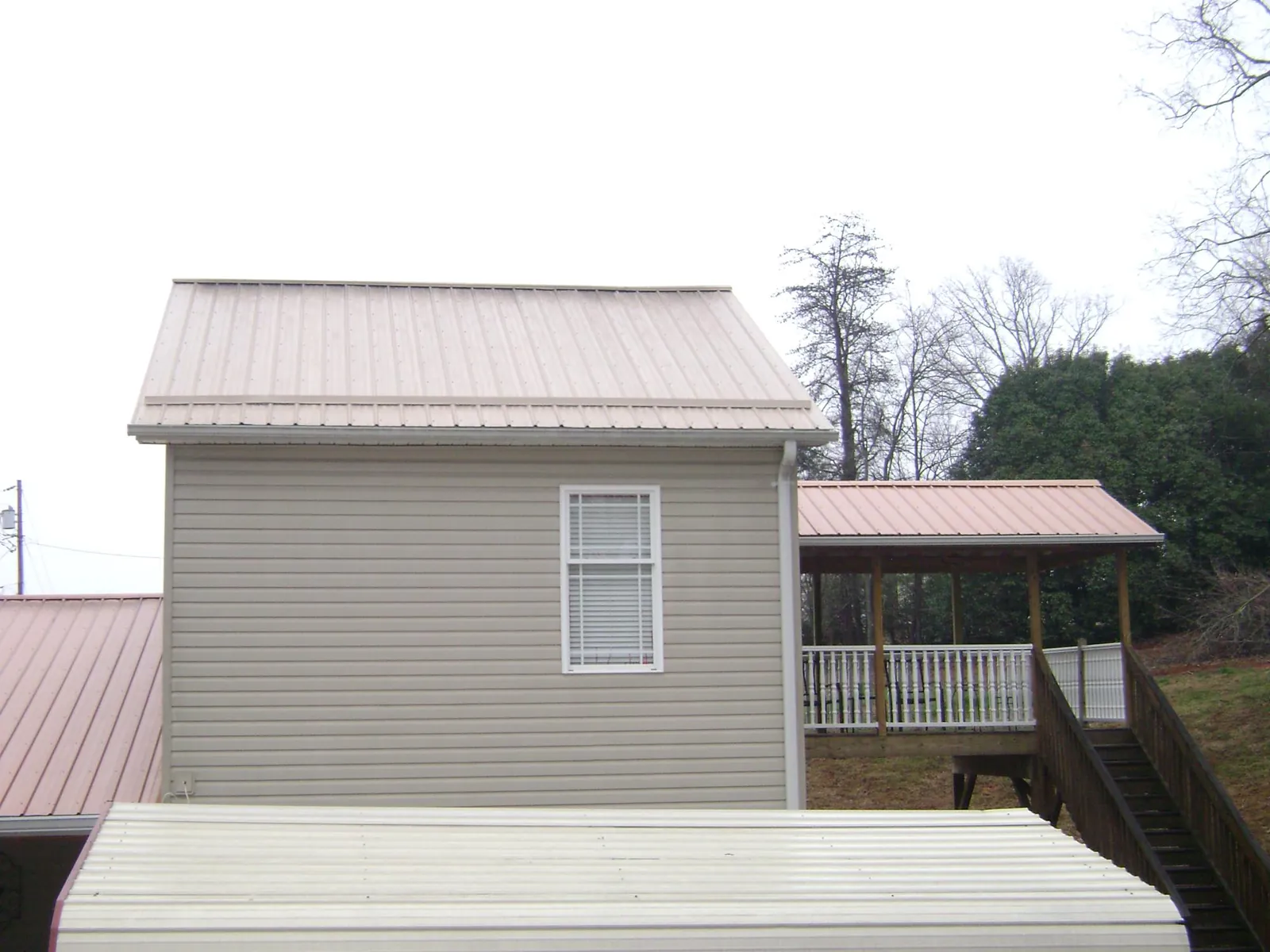 Tan metal roofs on a two story addition and attached porch, from a Roof Replacement job in Lee Center